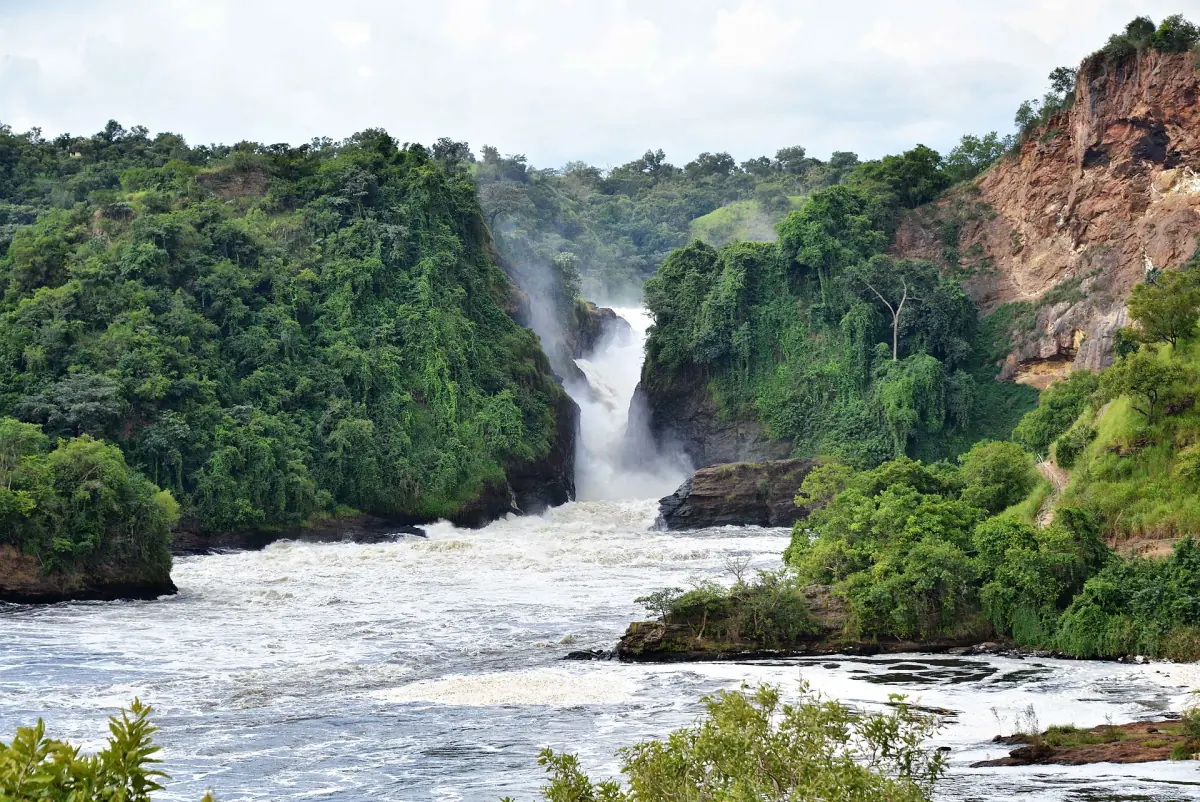Der Wasserfall fällt zwischen bewaldeten Felswänden in den brodelnden Nil